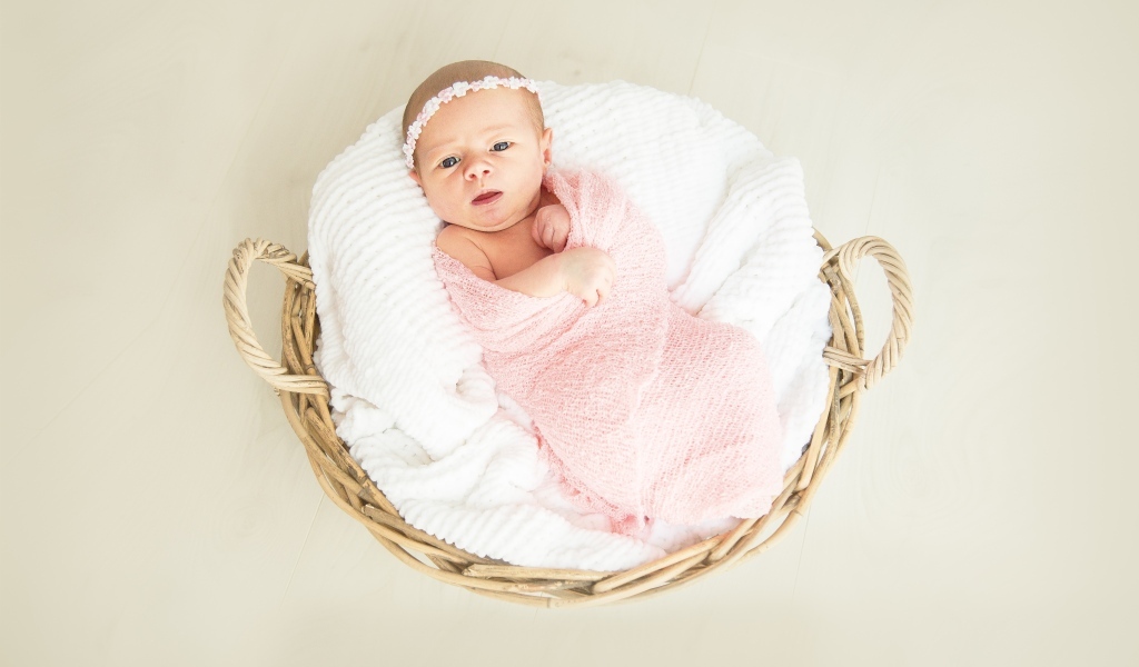 Новорожденная девочка в розовом покрывале в корзине