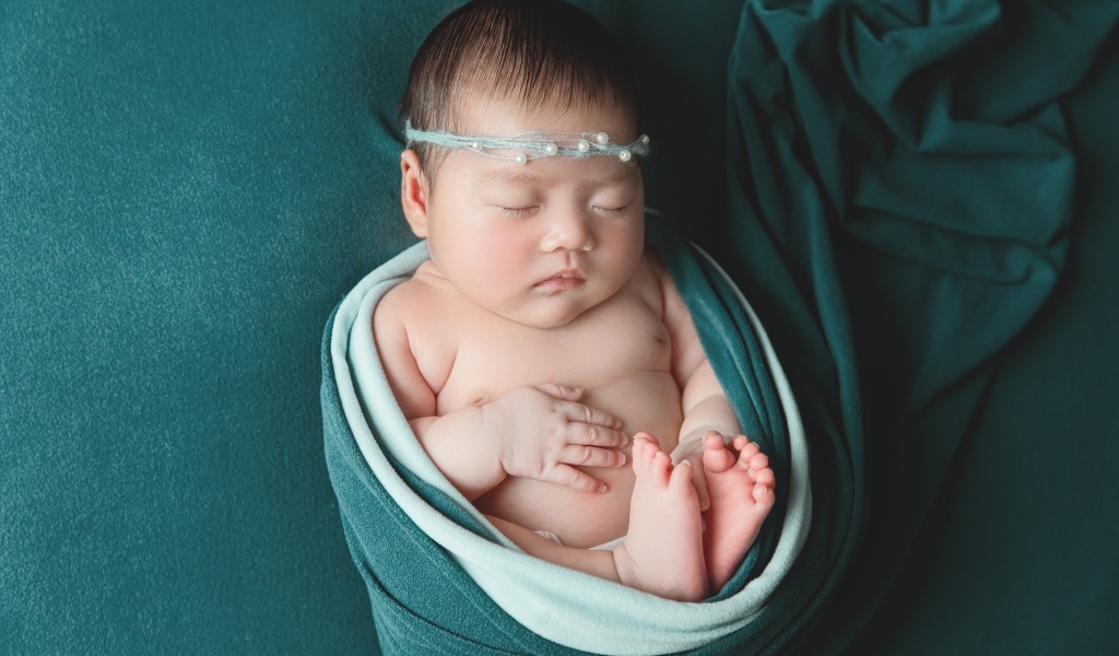 Фотография спящей новорожденной девочки на зеленом фоне