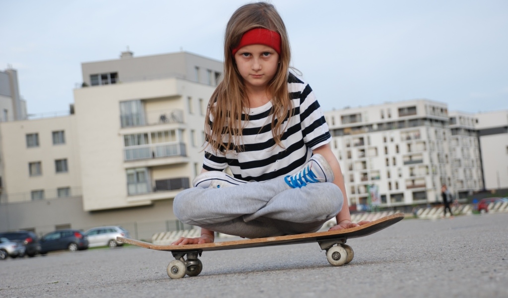 Серьезная девочка сидит на  скейтборде