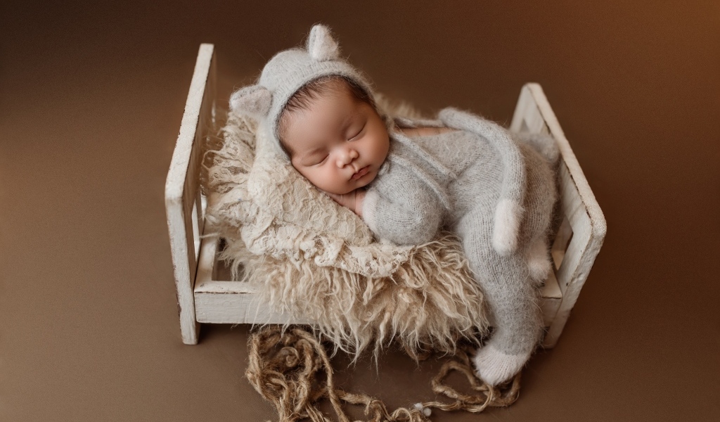 Спящий ребенок на маленькой кровати на коричневом фоне