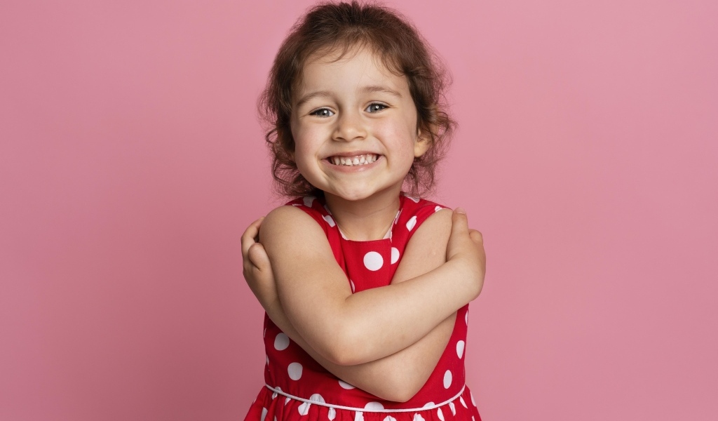 Улыбающаяся маленькая девочка в красном платье на розовом фоне