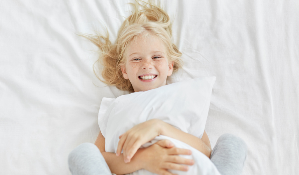 Улыбающаяся маленькая девочка с подушкой на кровати