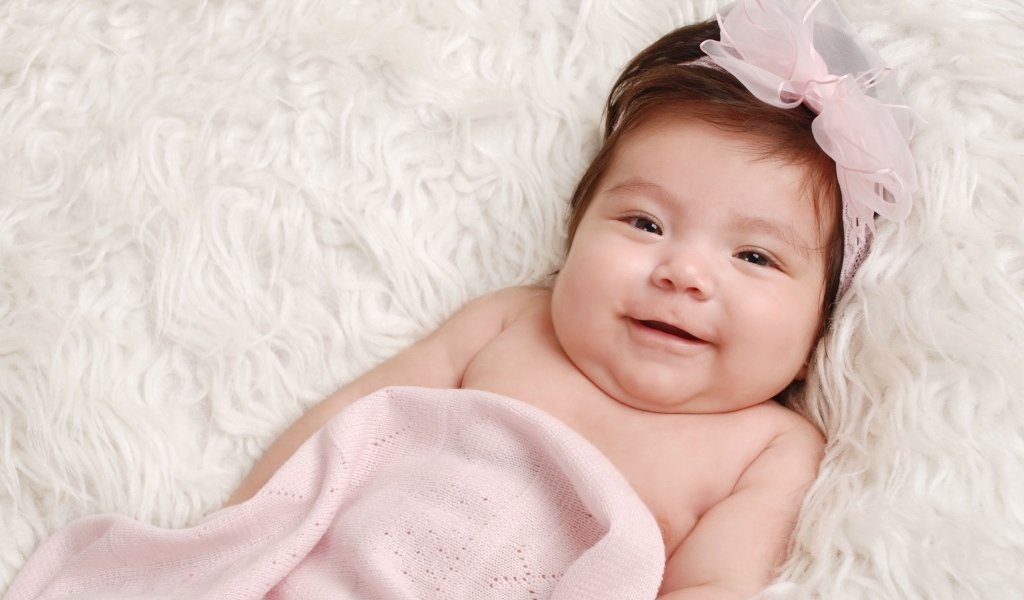 Улыбающаяся новорожденная малышка с бантом на голове