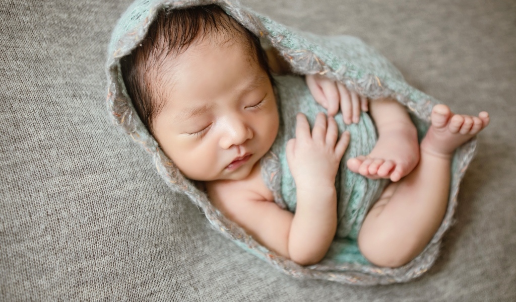 Крошечный новорожденный малыш на сером фоне