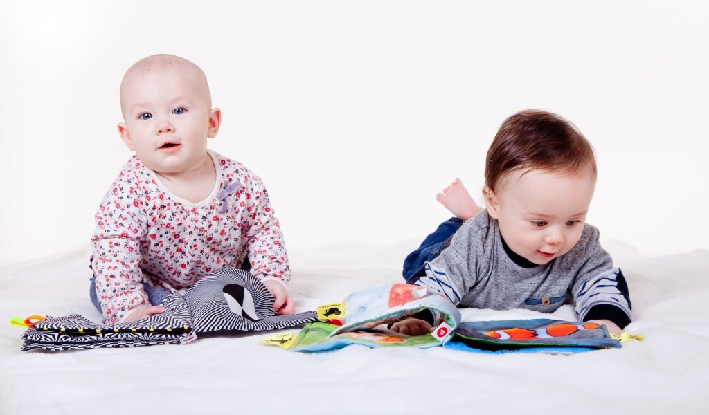 Два маленьких ребенка на кровати с мягкими книгами