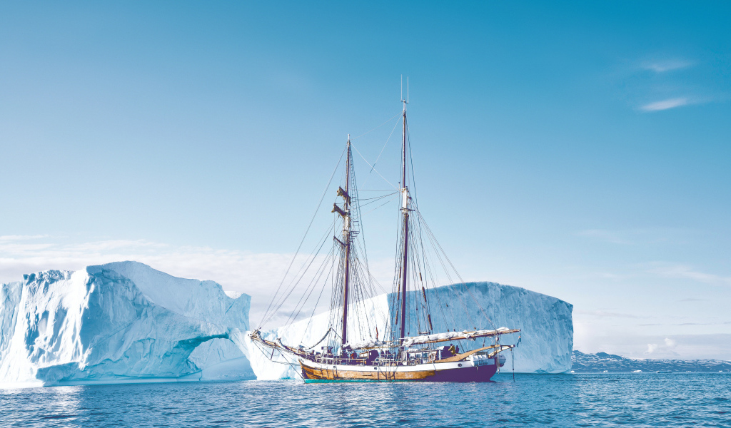 Большой корабль подплывает к голубому айсбергу в море