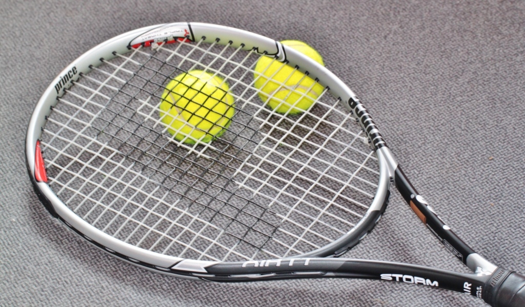 Ракетка и два мяча для тенниса на сером столе