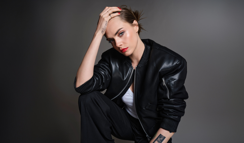 Актриса Кара Делевинь в черной кожаной куртке на сером фоне