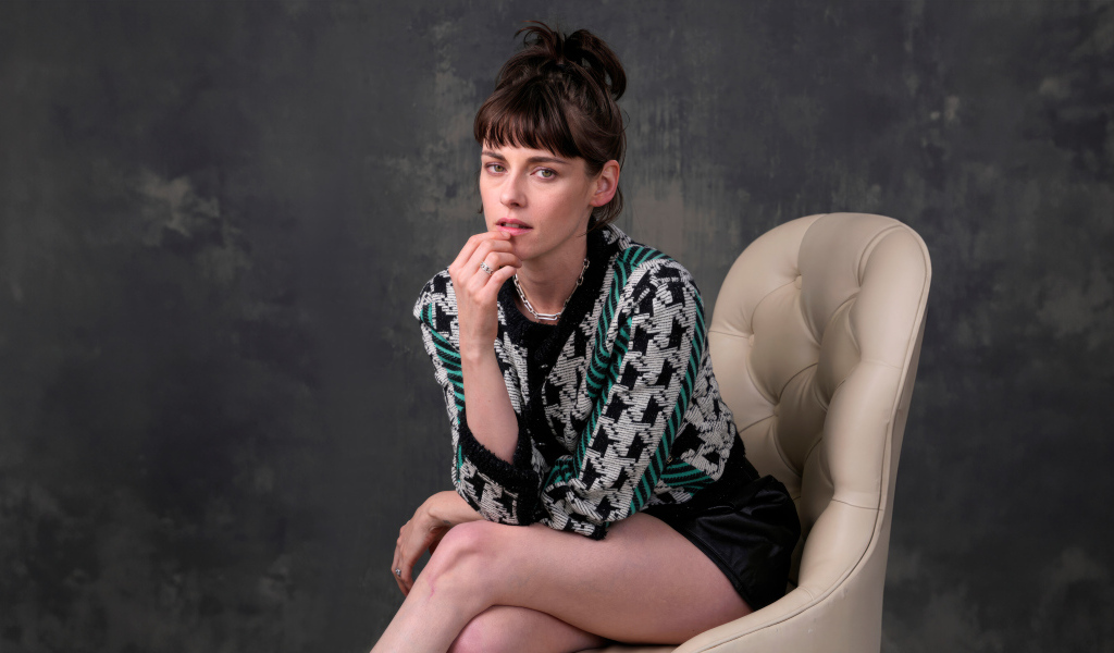 Актриса Кристен Стюарт сидит в кресле на фоне серой стены