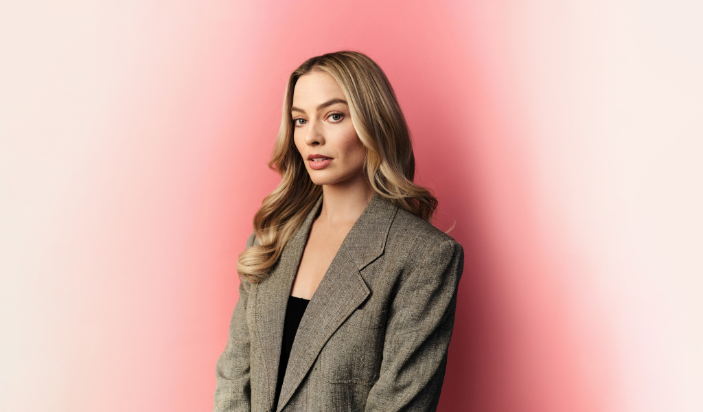Актриса Марго Робби в сером пиджаке на розовом фоне
