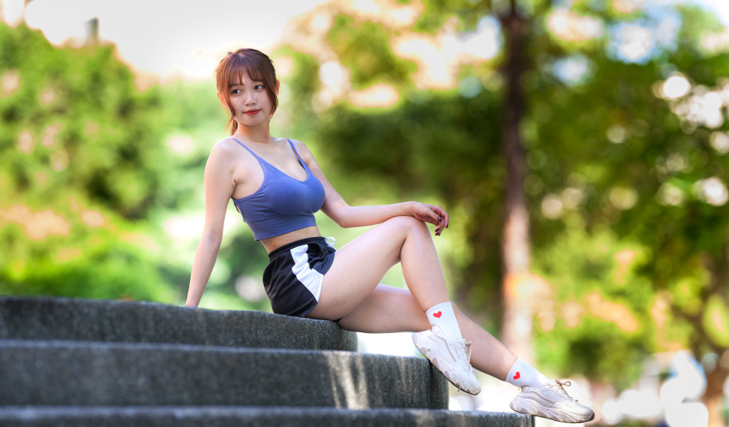 Спортивная азиатка в кроссовках сидит на ступеньках