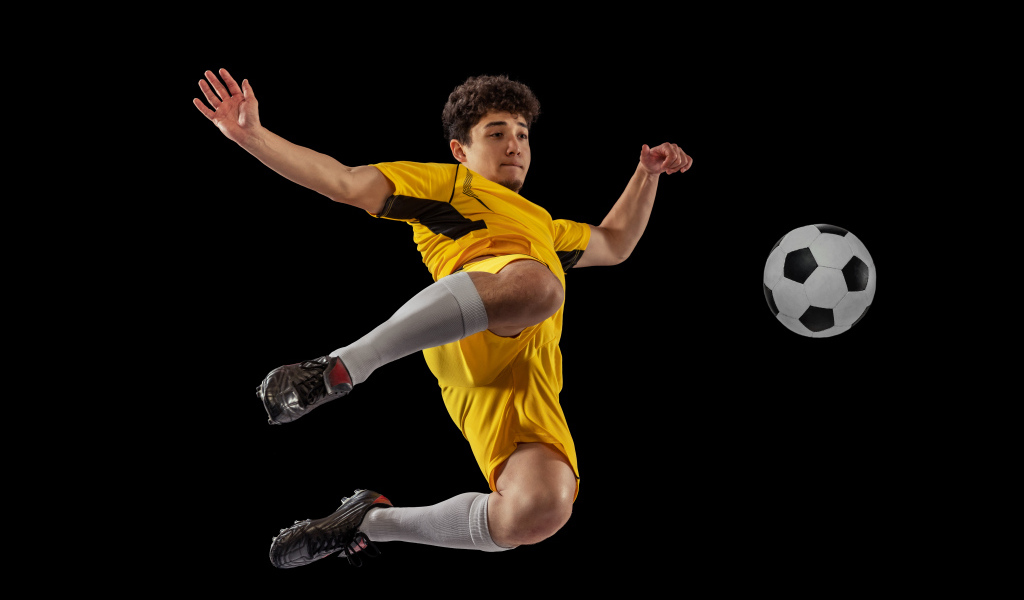 Мужчина футболист отбивает мяч на черном фоне
