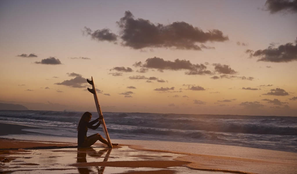 Девушка серфингистка сидит на берегу моря