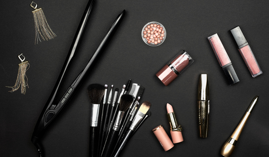 Кисточки с косметикой и плойкой на черном фоне