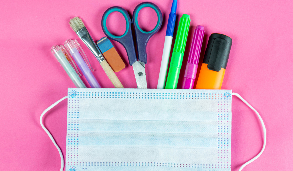 Канцелярские предметы и медицинская маска на розовом фоне