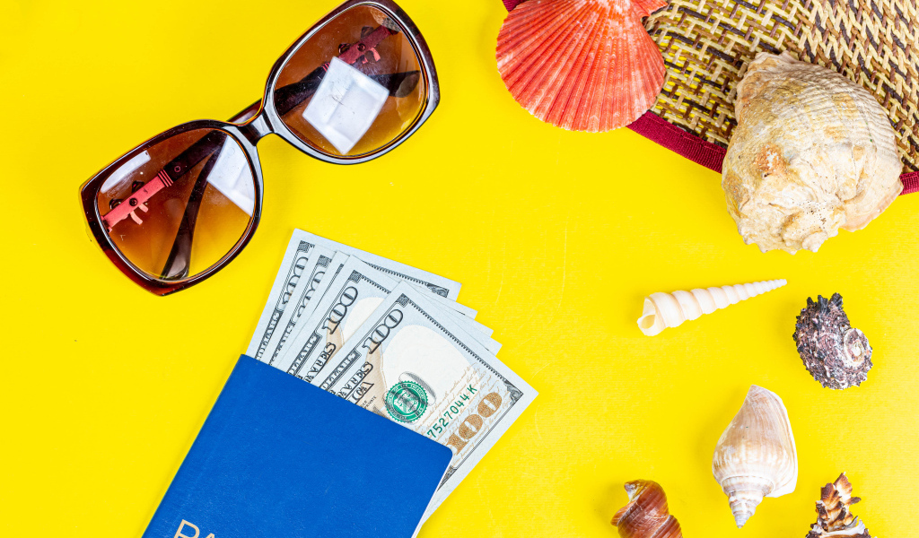 Очки, доллары с паспортом и ракушки на желтом фоне