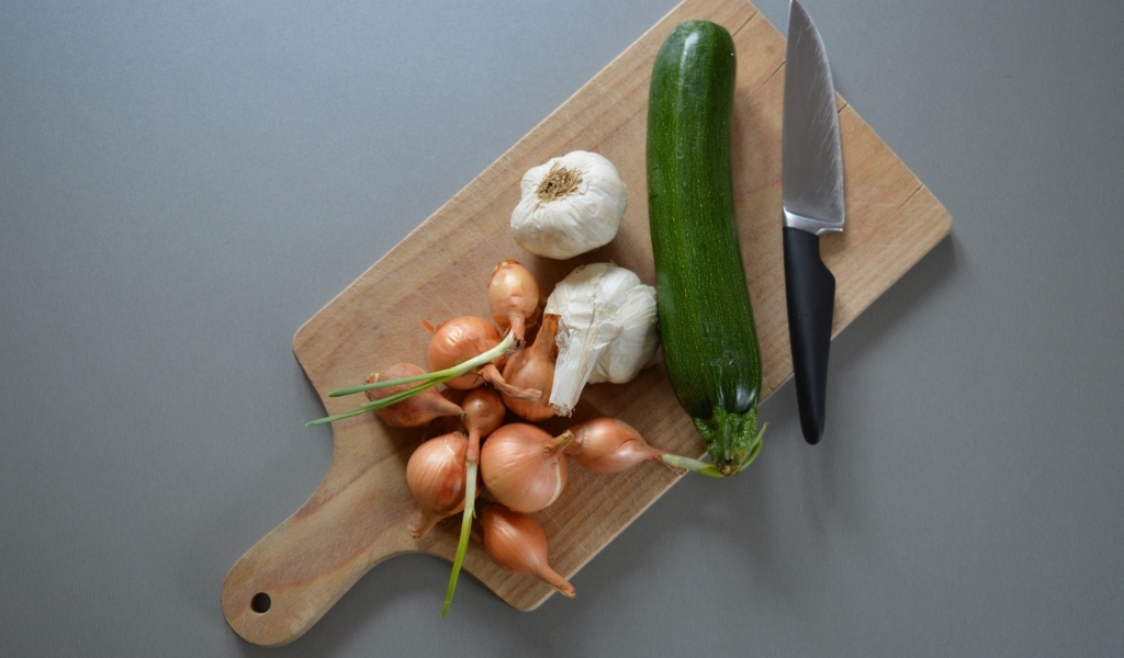 Лук, чеснок и кабачок на разделочной доске с ножом