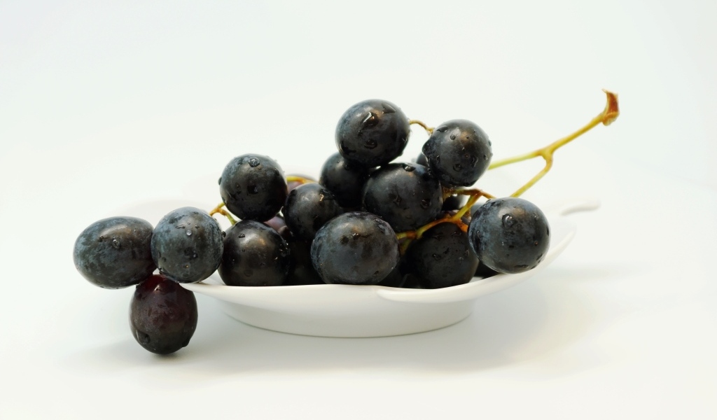 Гроздь синего винограда в тарелке на белом фоне