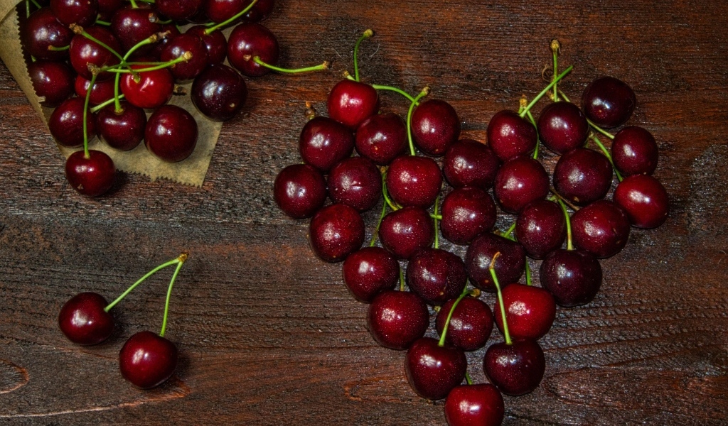 Сердце из спелых ягод черешни на деревянном столе
