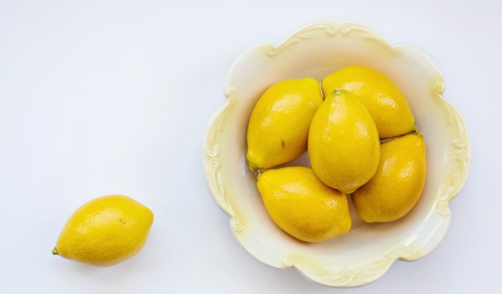 Много желтых лимонов в тарелке на сером фоне