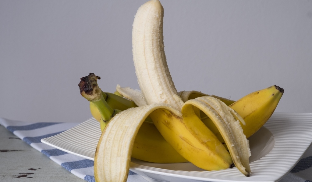 Очищенный банан на тарелке на сером фоне