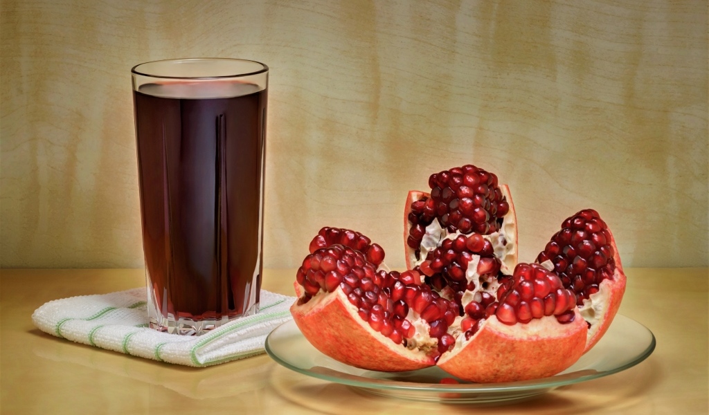 Красный гранат на столе со стаканом сока