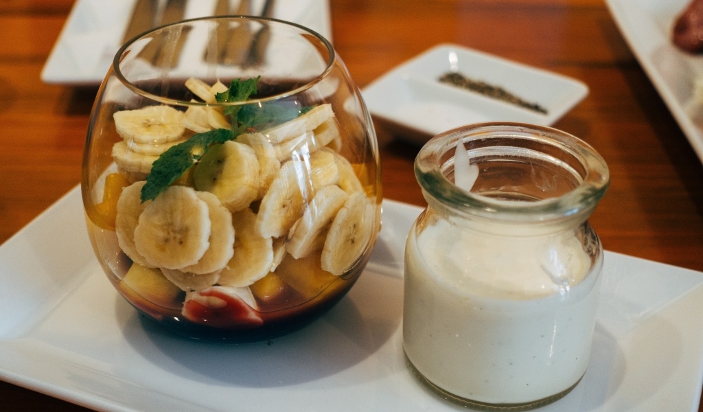 Нарезанные бананы в стакане на столе с йогуртом