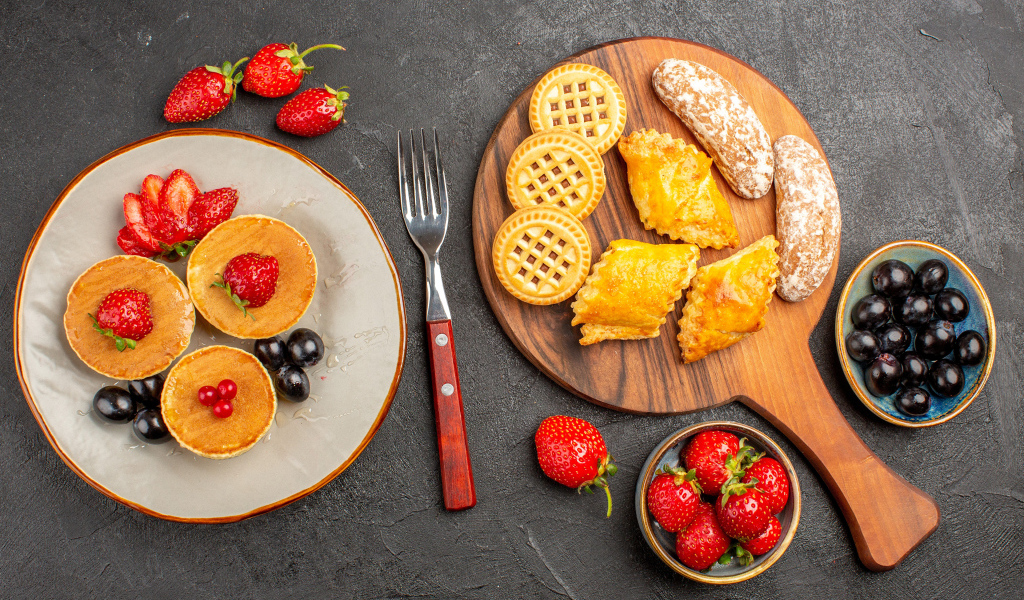 Печенье и оладьи на столе с ягодами клубники и виноградом