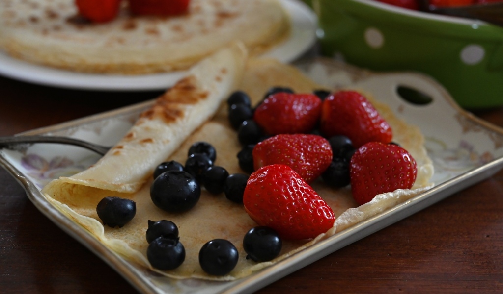 Блин с ягодами черники и клубники на тарелке