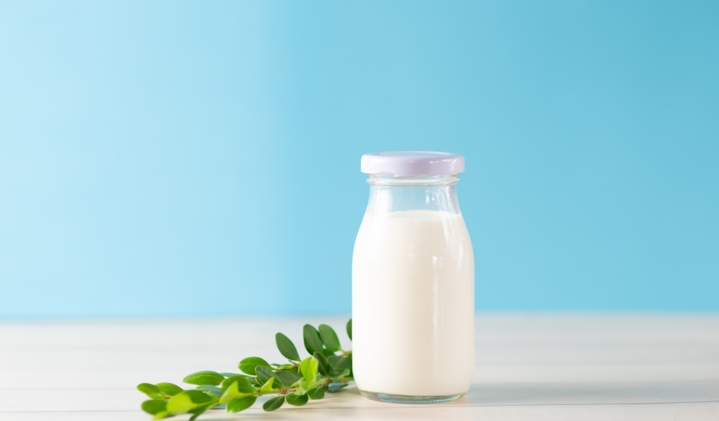 Бутылка молока с листьями на голубом фоне