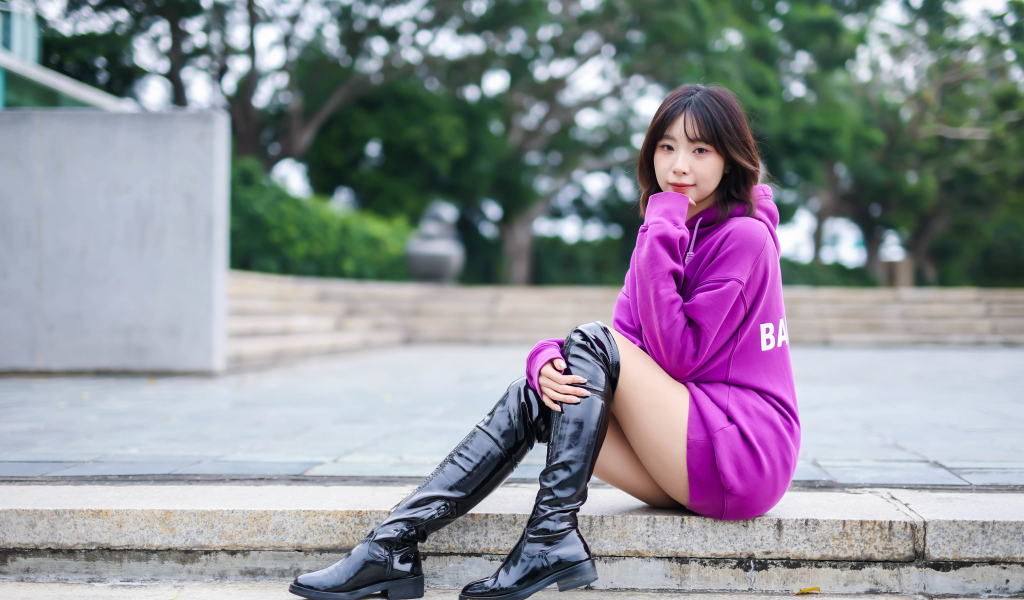 Девушка азиатка в длинных черных сапогах сидит на ступенях