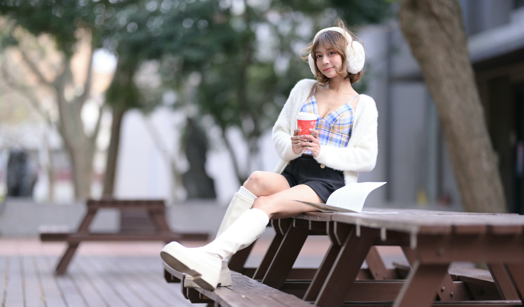 Девушка азиатка с кофе сидит на столе в парке