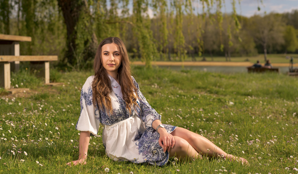 Красивая девушка в платье сидит на зеленой траве в парке