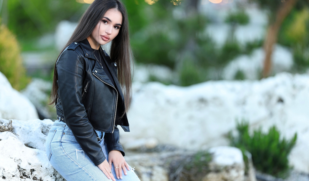 Брюнетка в черной кожаной куртке сидит на камне