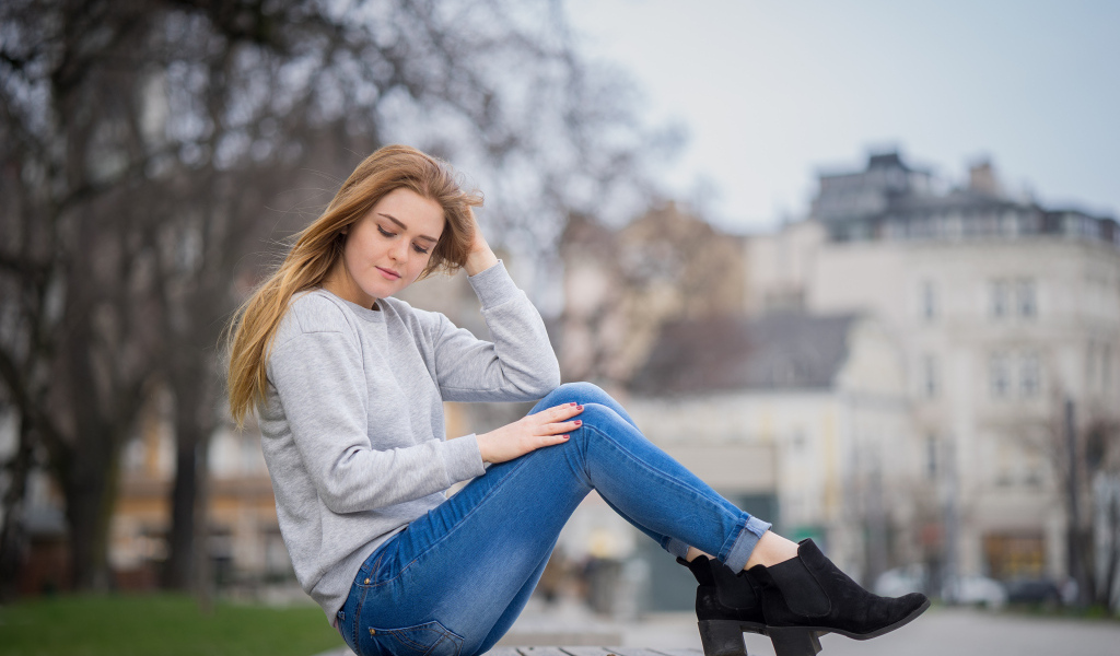 Милая девушка в синих джинсах сидит на лавке