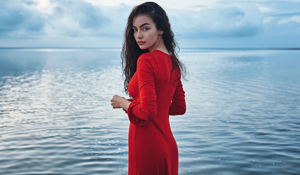 Милая девушка в красном платье стоит у воды