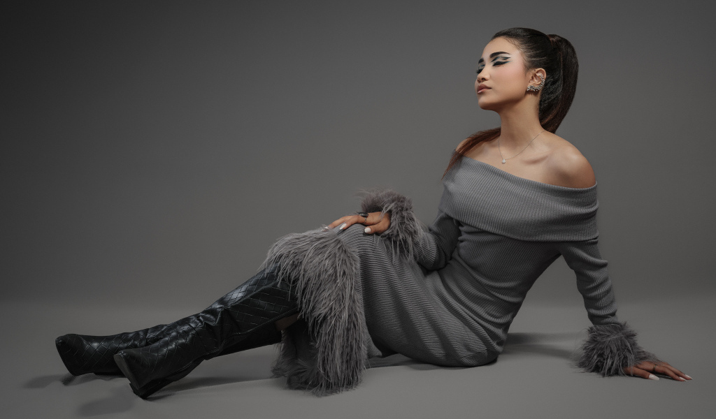 Девушка в платье и длинных черных сапогах на сером фоне