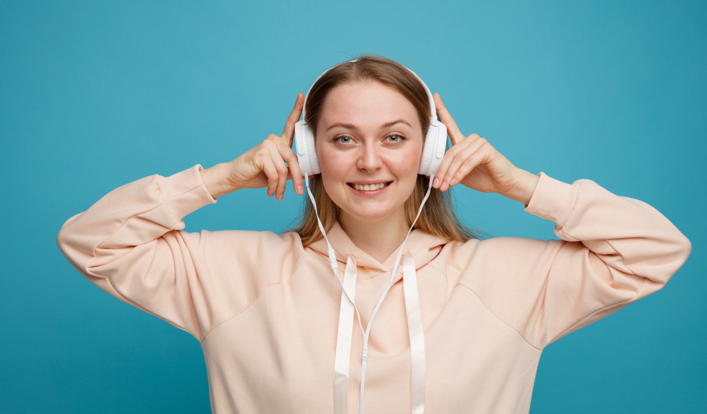Улыбающаяся девушка в наушниках на голубом фоне