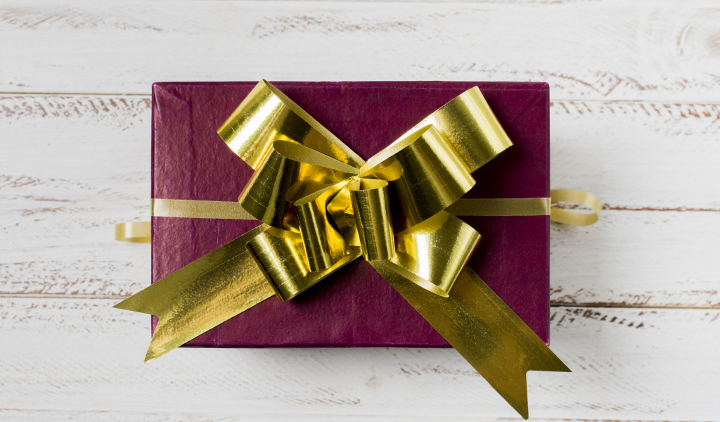 Красная коробка с подарком с золотым бантом на столе