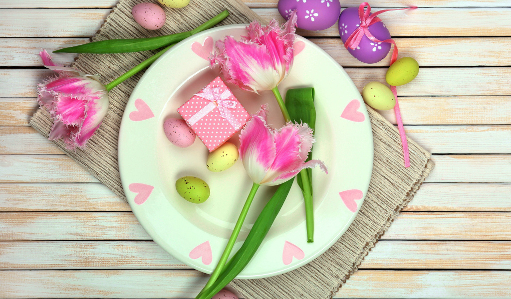 Пасхальные яйца с тюльпанами на тарелке на столе