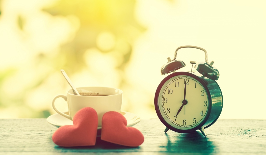 Будильник на столе с чашкой кофе и сердечками