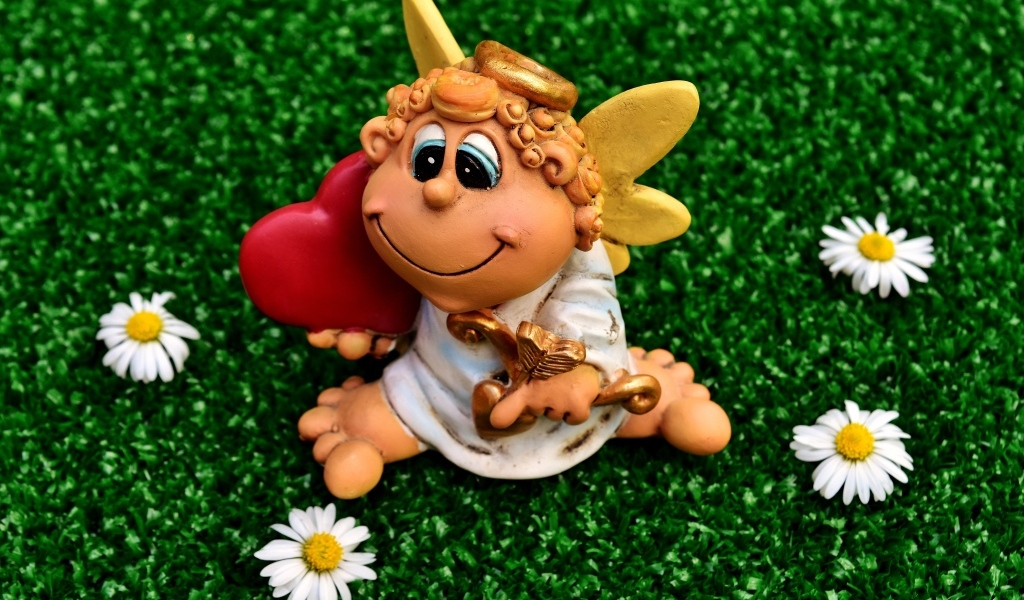 Статуэтка ангела на зеленой траве с белыми ромашками