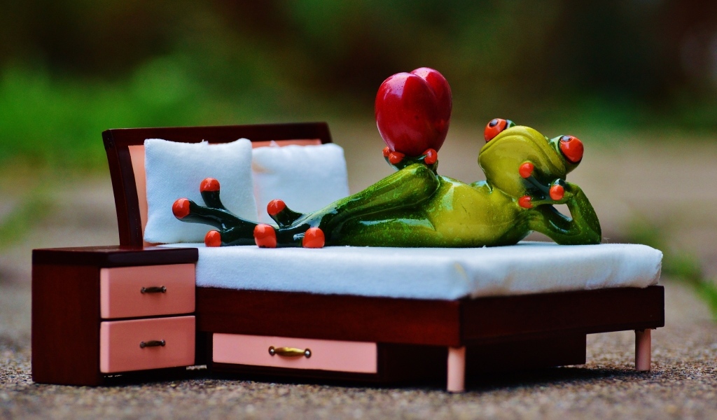 Фигурка зеленая лягушка с красным сердцем на кровати