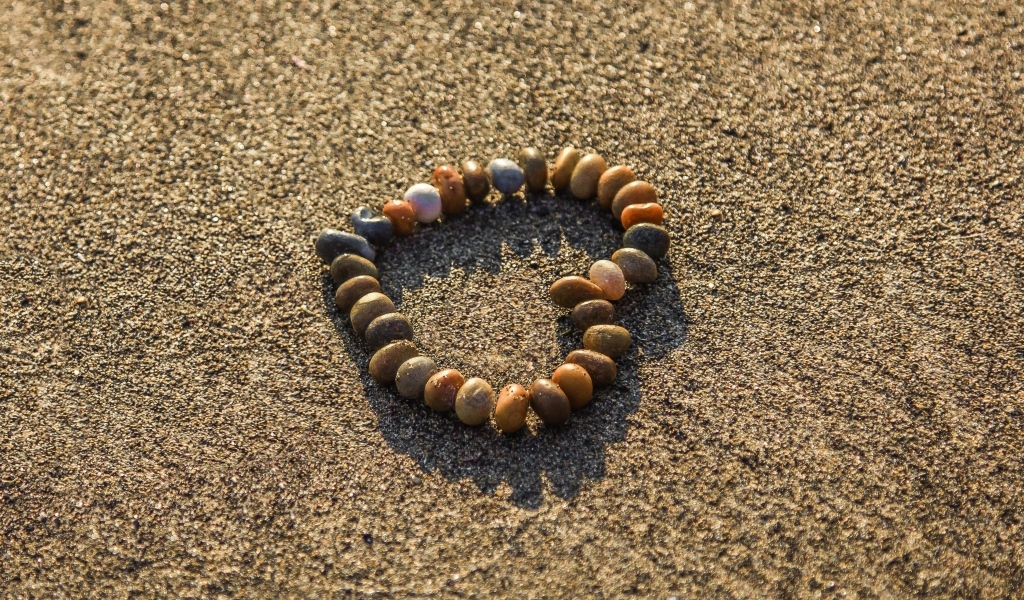 Сердце из камней на морском песке летом