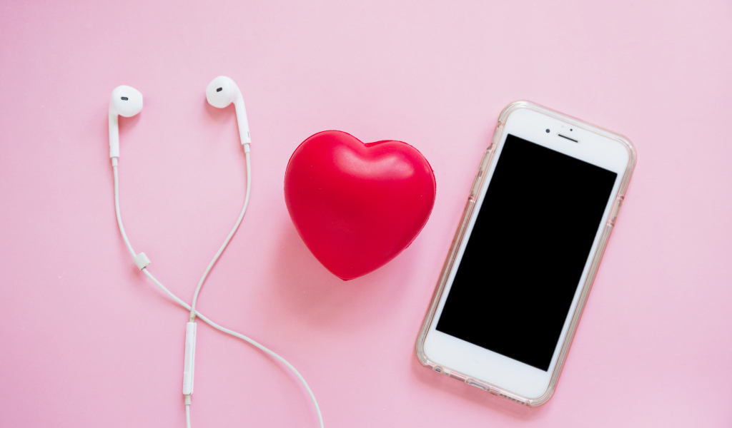 Телефон, наушники и красное сердце на розовом фоне