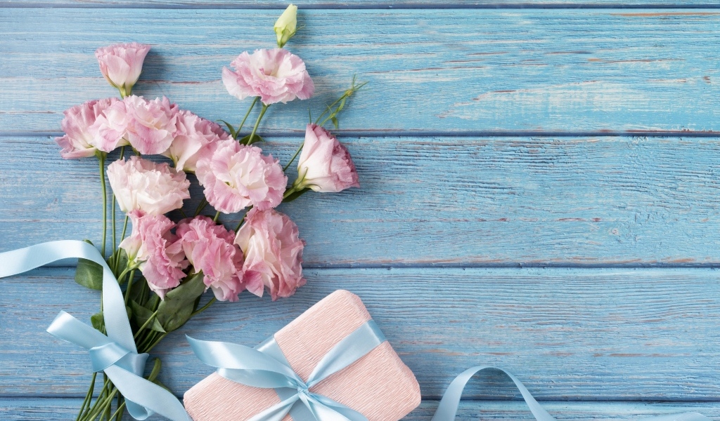 Букет розовых цветов эустомы с подарком на голубом столе