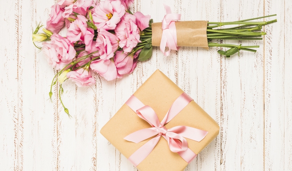 Букет розовых цветов эустомы с подарком на деревянном фоне