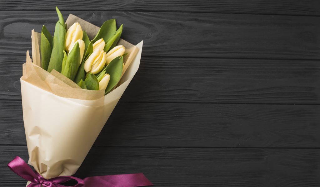 Букет желтых тюльпанов в бумаге на черном столе