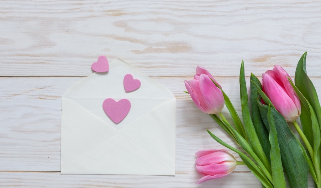Розовые тюльпаны с конвертом с сердечками на деревянном фоне