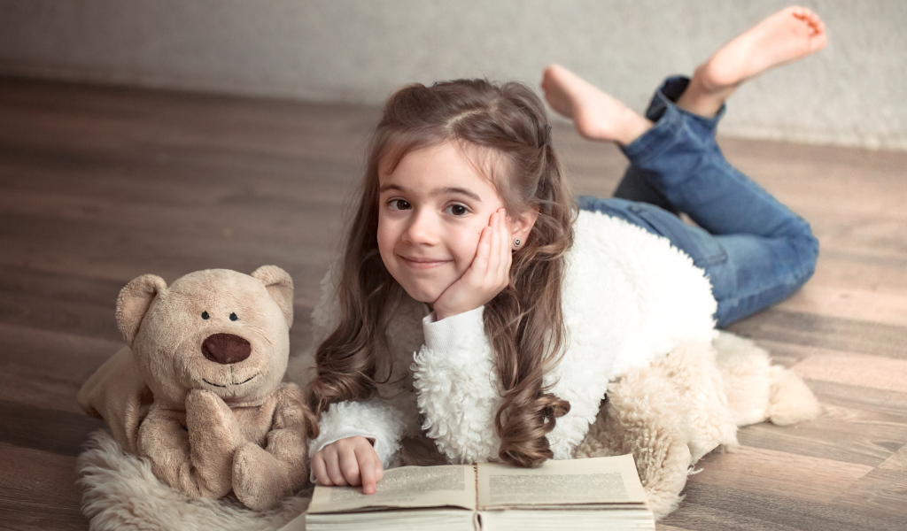 Девочка с медведем и книгой лежит на полу
